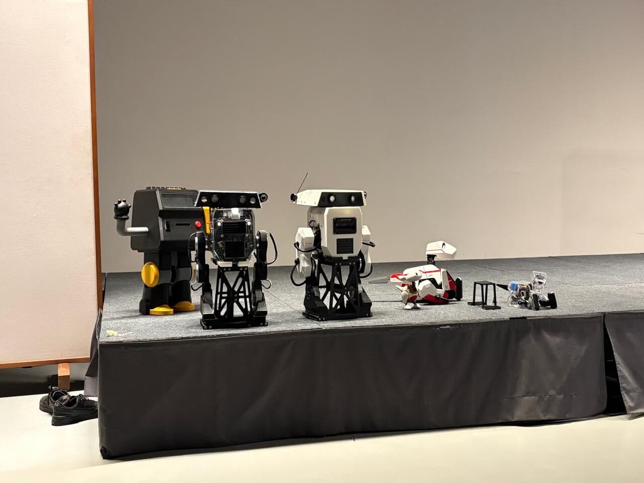 Four robots of different sizes lined up on a low stage at a public showcase.